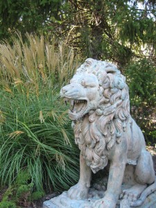 Life size lion statue  in garden  surrounded with maiden grass.